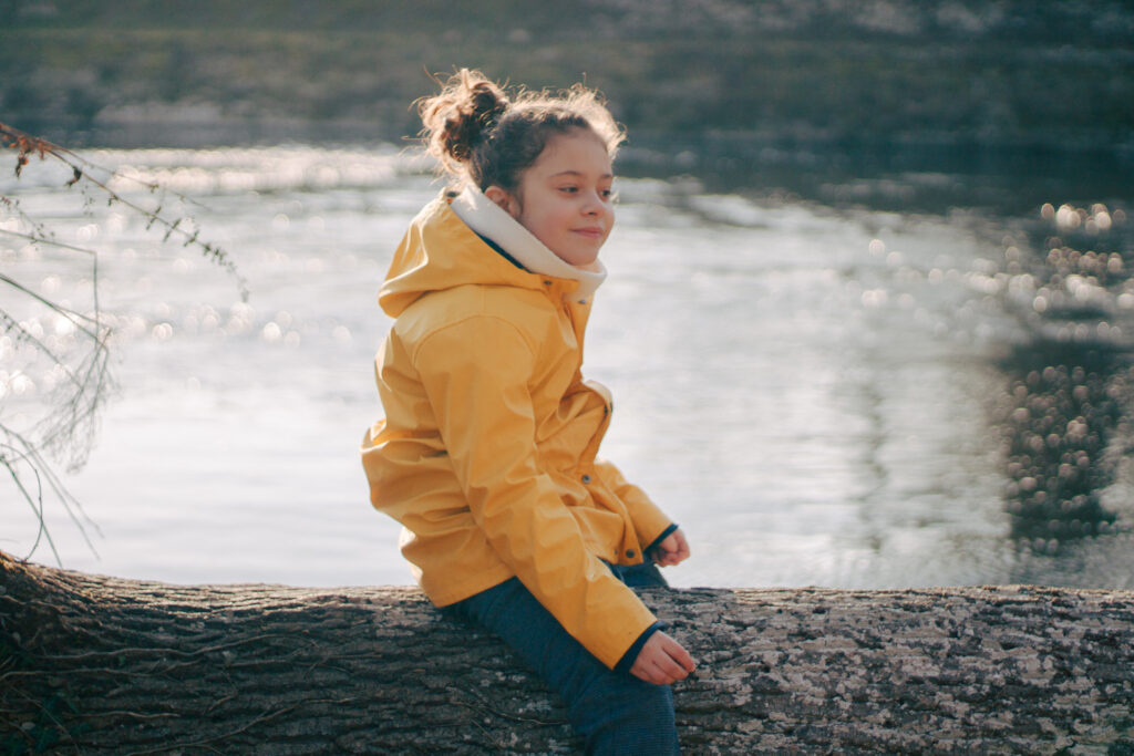 Petite fille assise sur un tron d'arbre au bord de l'eau au parc des iles de Vermenton dans l'yonne.