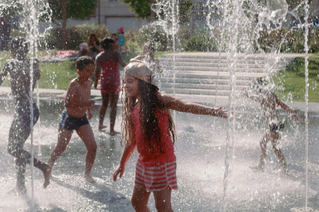 Enfant s’amusant sur le miroir d’eau à Reims, éclaboussures et reflets du ciel d’été autour d’elle