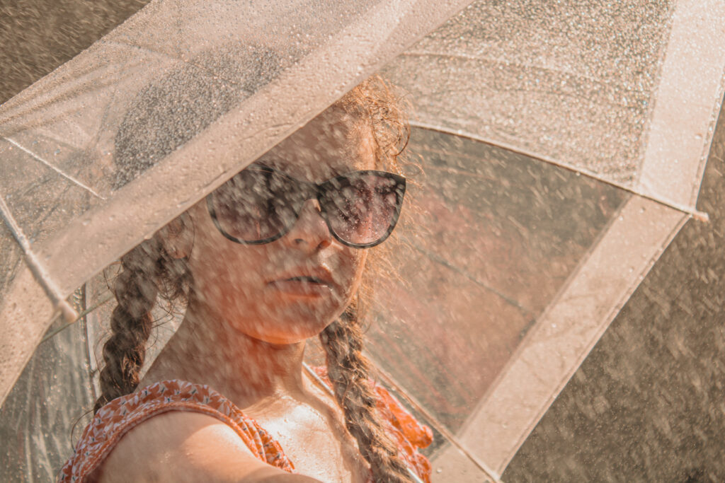 Enfant sous un parapluie transparent arrosé dans un jardin de l’Yonne, lumière dorée du soir, souvenir joyeux d’un été en famille près d’Auxerre.