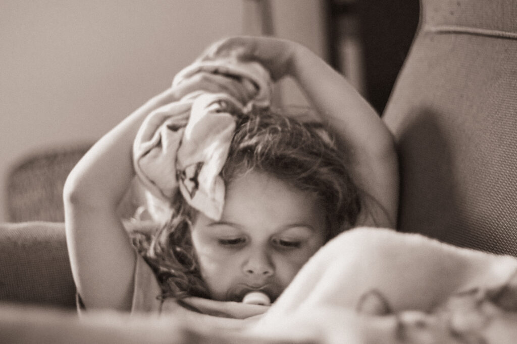 Portrait en noir et blanc d’une petite fille avec sa tétine, absorbée par la lecture d’un livre, instant doux et silencieux, à Venoy près d'Auxerre dans l'Yonne.
