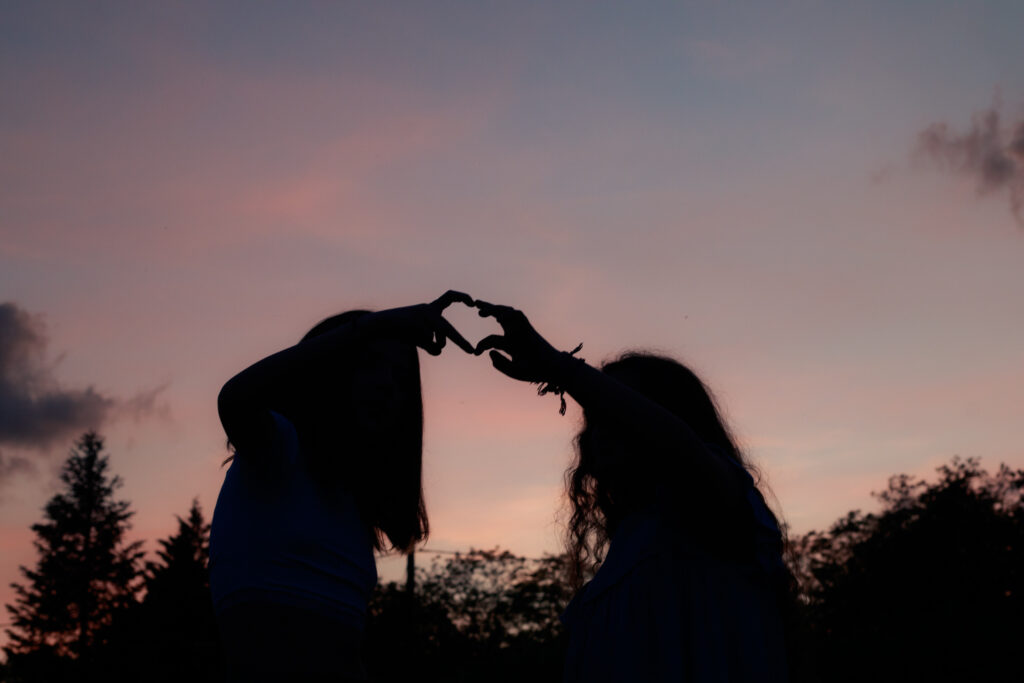 Deux amies formant un cœur avec leurs mains en ombre portée, photographiées au crépuscule dans l’Yonne, souvenir d’un été près d’Auxerre.