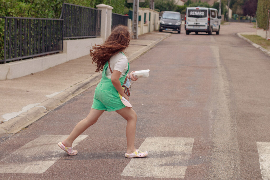 Petite fille en salopette short verte traversant un passage piéton en été, tenant des mûres fraîchement cueillies, près d'Auxerre dans l'Yonne.
