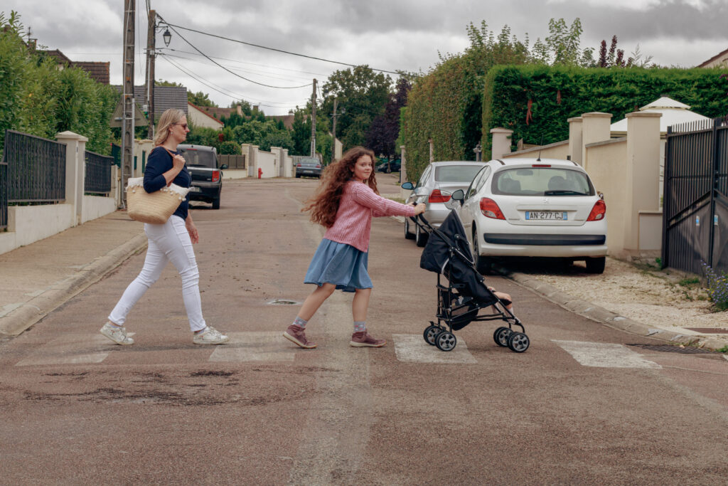 Petite fille traversant un passage piéton accompagnée de sa tante, poussant une poussette où se trouve sa cousine à Auxerre.