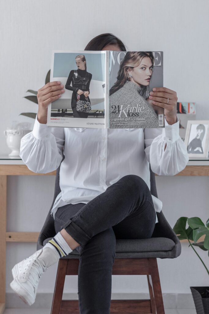 Femme tenant un magazine ouvert sur des photos de mannequins, illustrant l’impact des standards irréalistes de beauté sur l’image de soi.