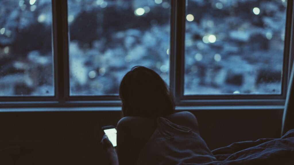 Femme regardant son téléphone d’un air mélancolique, symbolisant l’impact des réseaux sociaux sur l’image de soi.