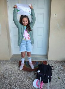 Petite fille posant devant la porte le jour de sa rentrée en CE2, souvenir parmi les photos de rentrée des classes