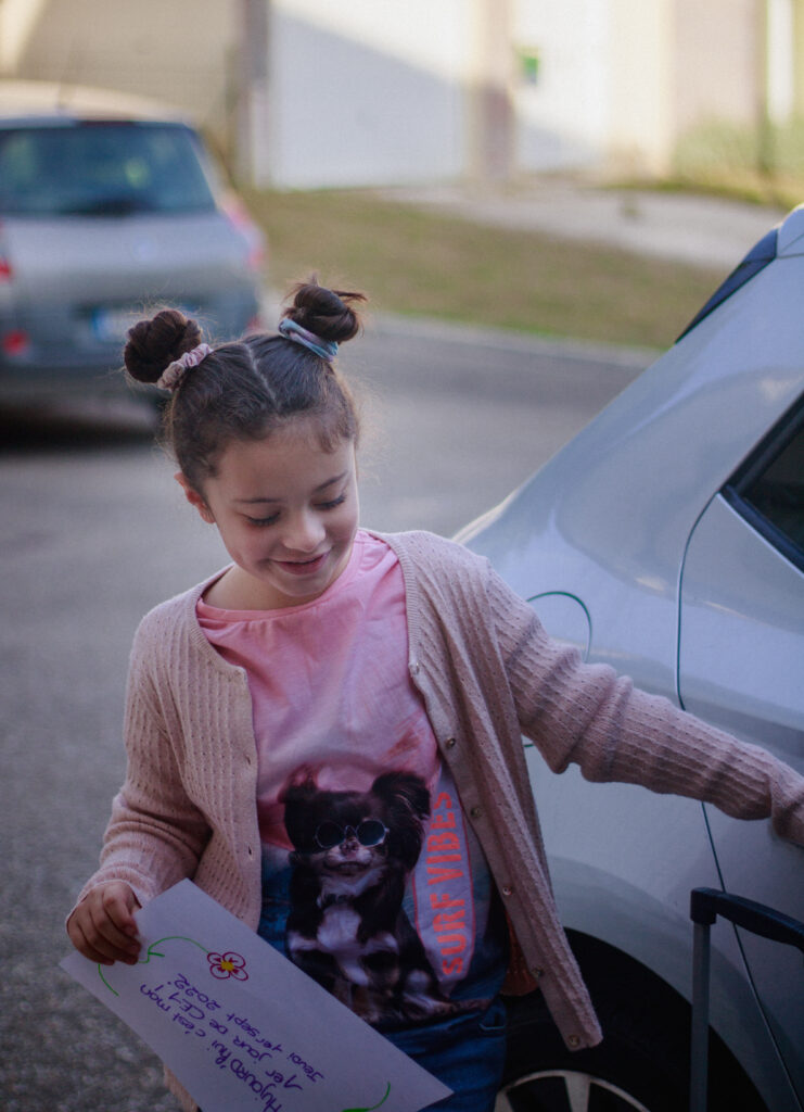 Petite fille souriante avec une pancarte “premier jour d’école” devant la maison