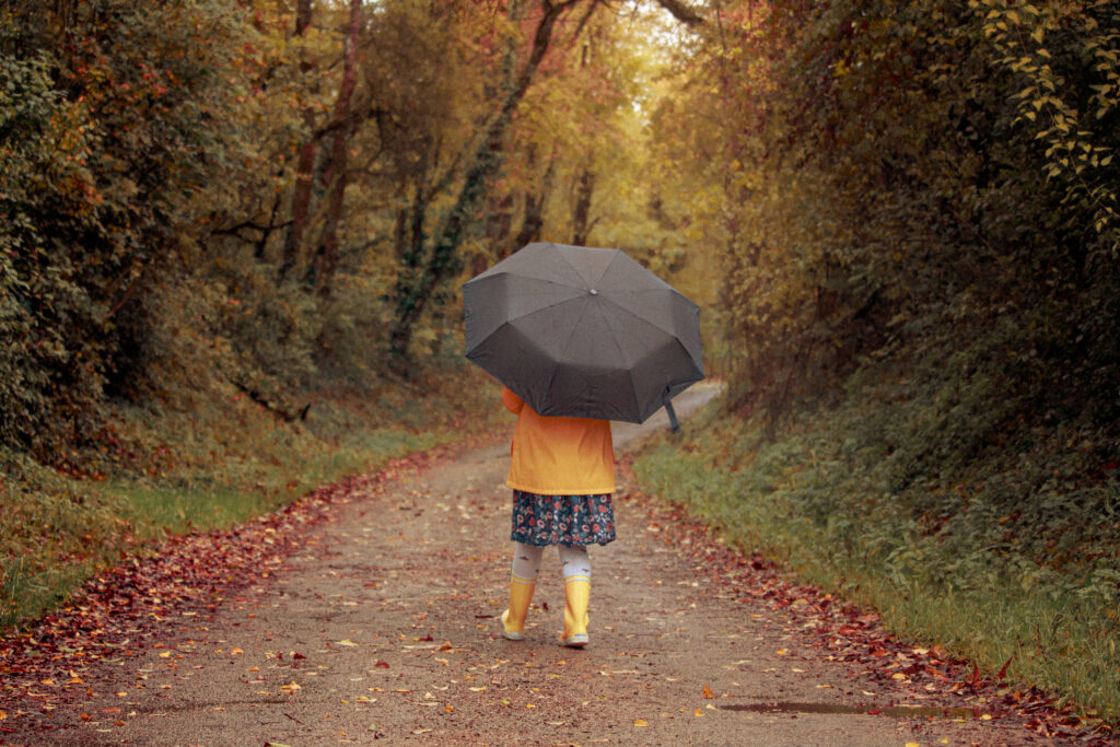 Petite fille en bottes de pluie se promenant dans la forêt automnale avec un parapluie.