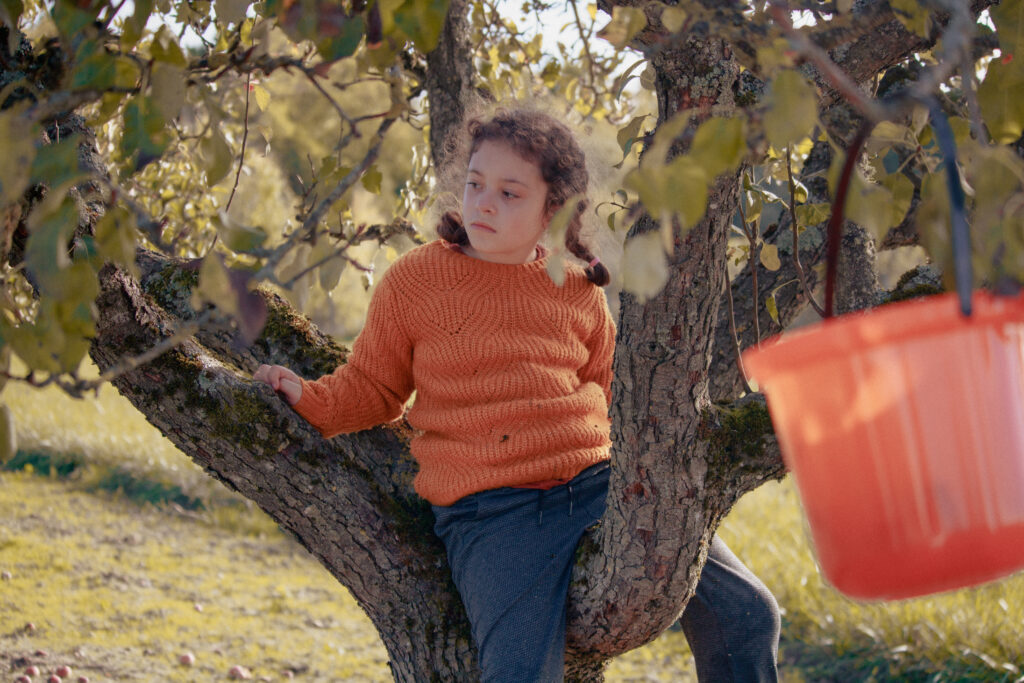 petite fille assise sur une branche d'arbre en automne.