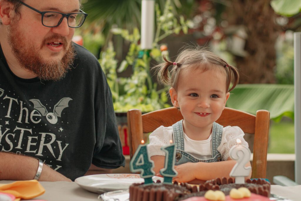 Moment de fête : un enfant de 2 ans et un adulte de 41 ans prêts à souffler leurs bougies sur un gâteau d’anniversaire, capturé de façon naturelle et spontanée.