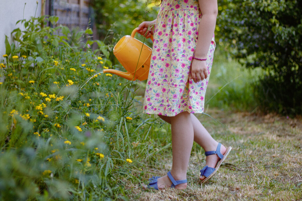 petite fille en robe printannière qui arrose les fleurs du jardin