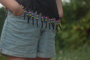 Détail d’un t-shirt à franges perlées DIY porté par une enfant, création réalisée avec des perles